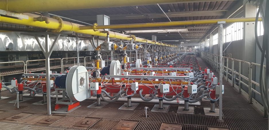 Impianto di produzione con tubazioni gialle e linee di macchinari in un ambiente industriale.